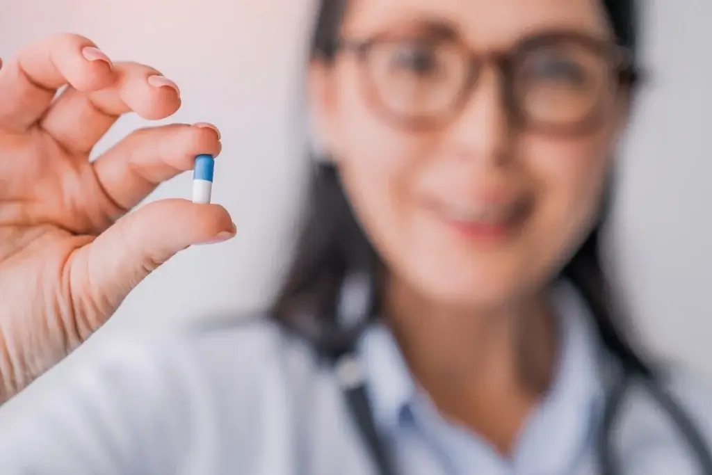 Close-up of a scientist holding a blue-and-white capsule, symbolizing dose optimization in oncology research under Project Optimus.